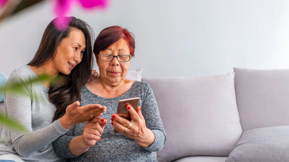 Adult daughter helping her mother use a phone on the couch