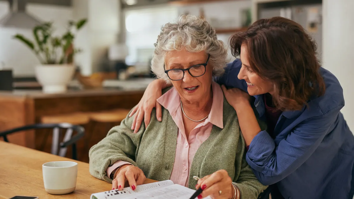 Adult daughter with her arm around her mother at the kitchen table, sharing a warm moment