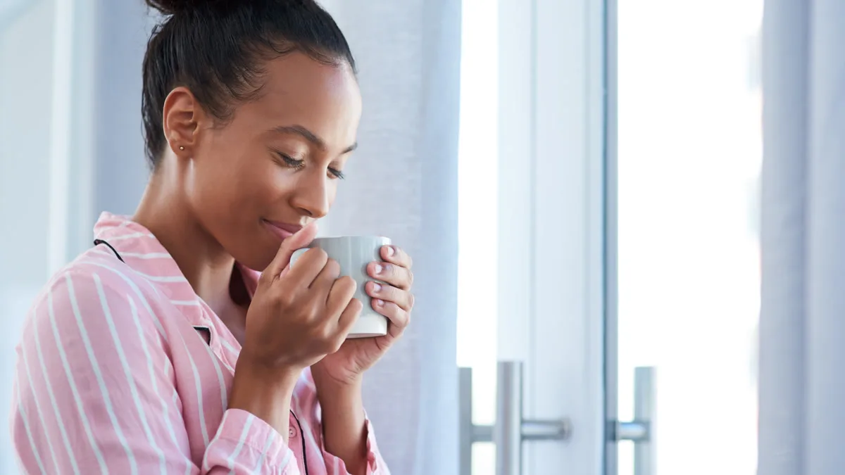 Person sitting comfortably in a sunlit apartment with a coffee mug and phone nearby