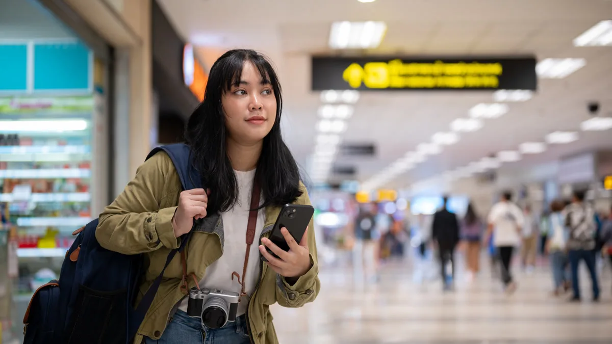 Solo traveler with backpack and phone walking through an airport terminal