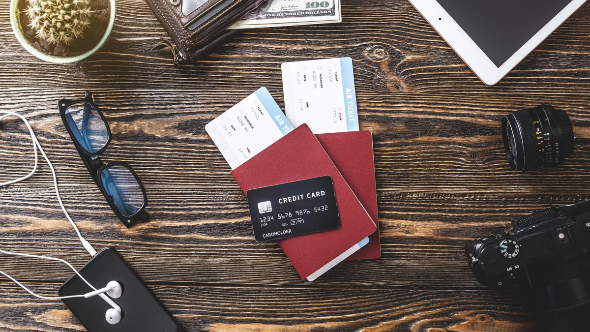 Flat lay of travel essentials: passport, boarding passes, credit card, camera, sunglasses, and tablet on a wooden table