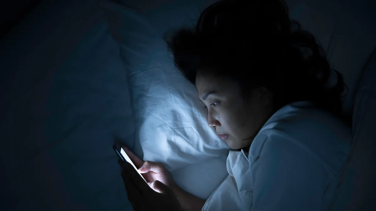 Person looking at their phone in bed at night, lit only by the screen