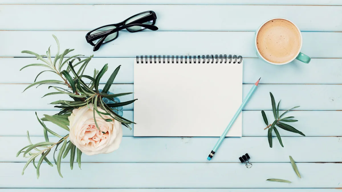 Flat lay of a notebook, coffee, glasses, and a pencil on a light blue wooden table